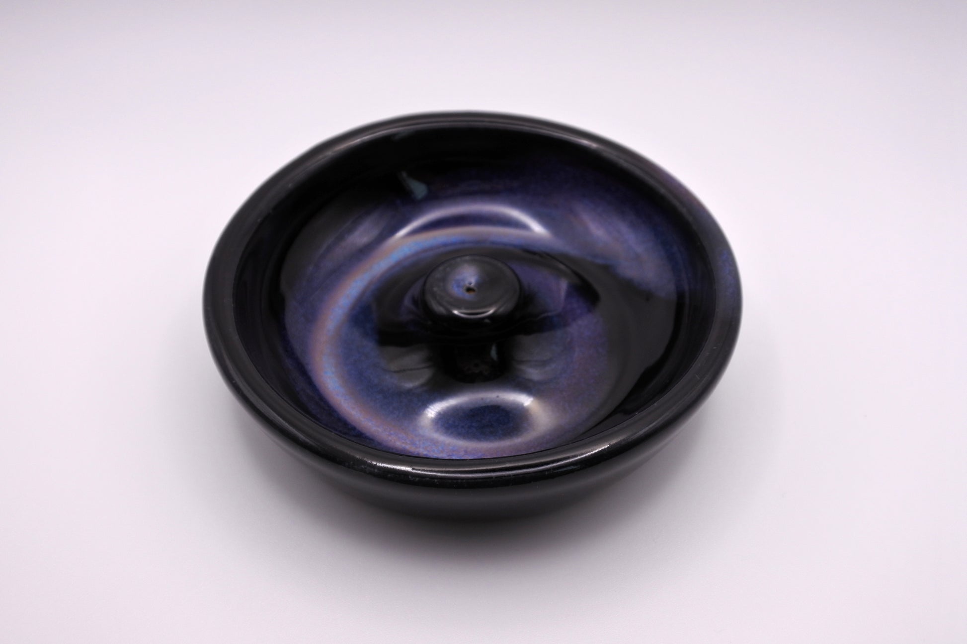 glossy black circular incense burner with a spiral of lavender, violet, coral, light blue, and blue glaze