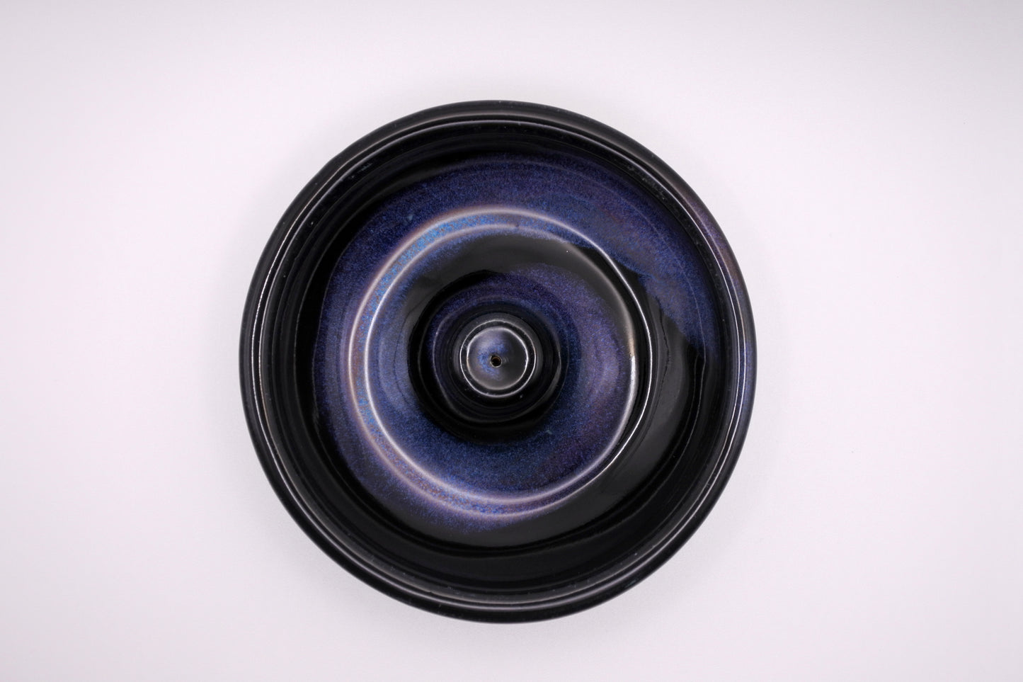 glossy black circular incense burner with a spiral of lavender, violet, coral, light blue, and blue glaze