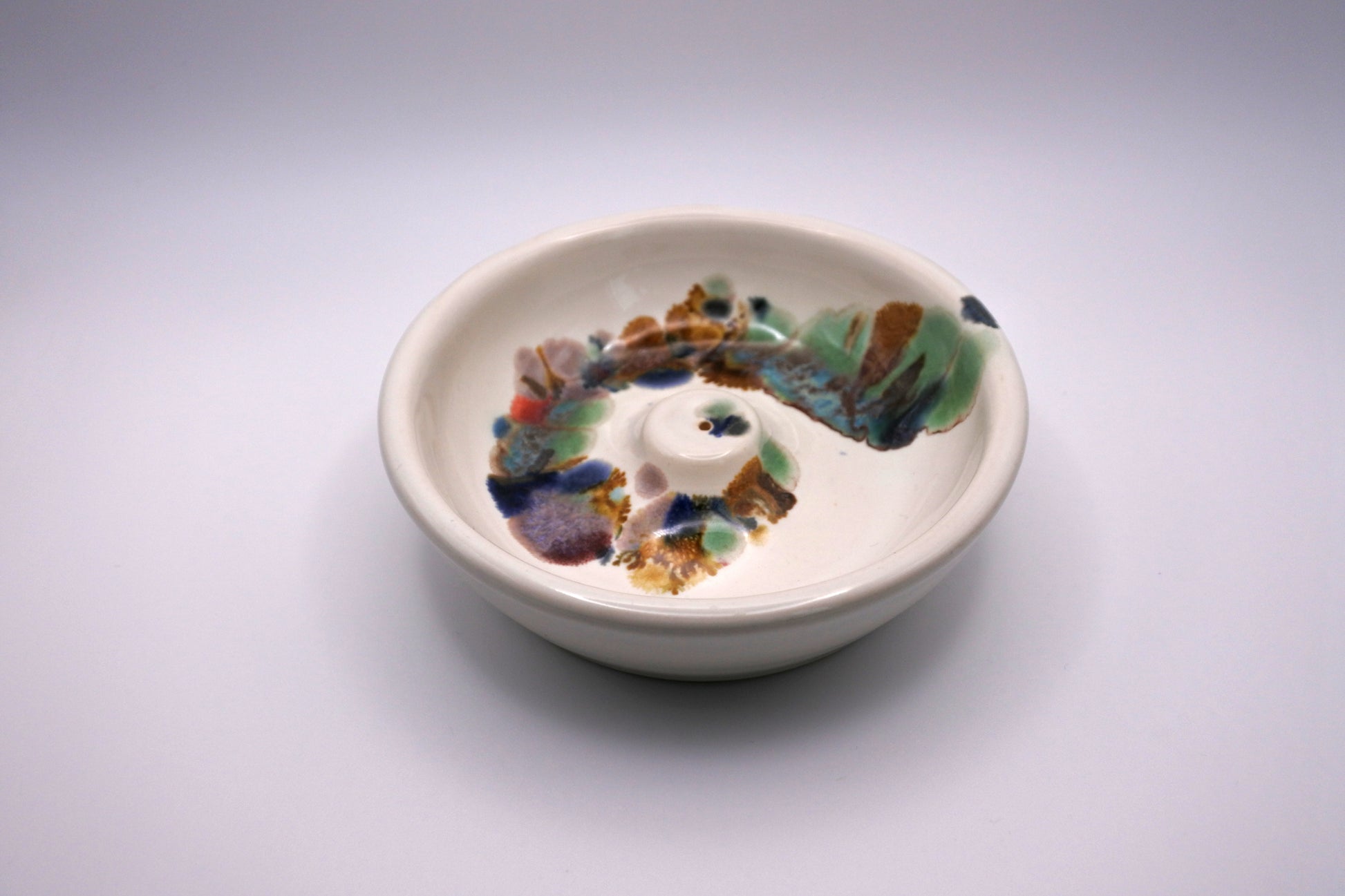 white circular incense burner with multi color drips in a spiral pattern