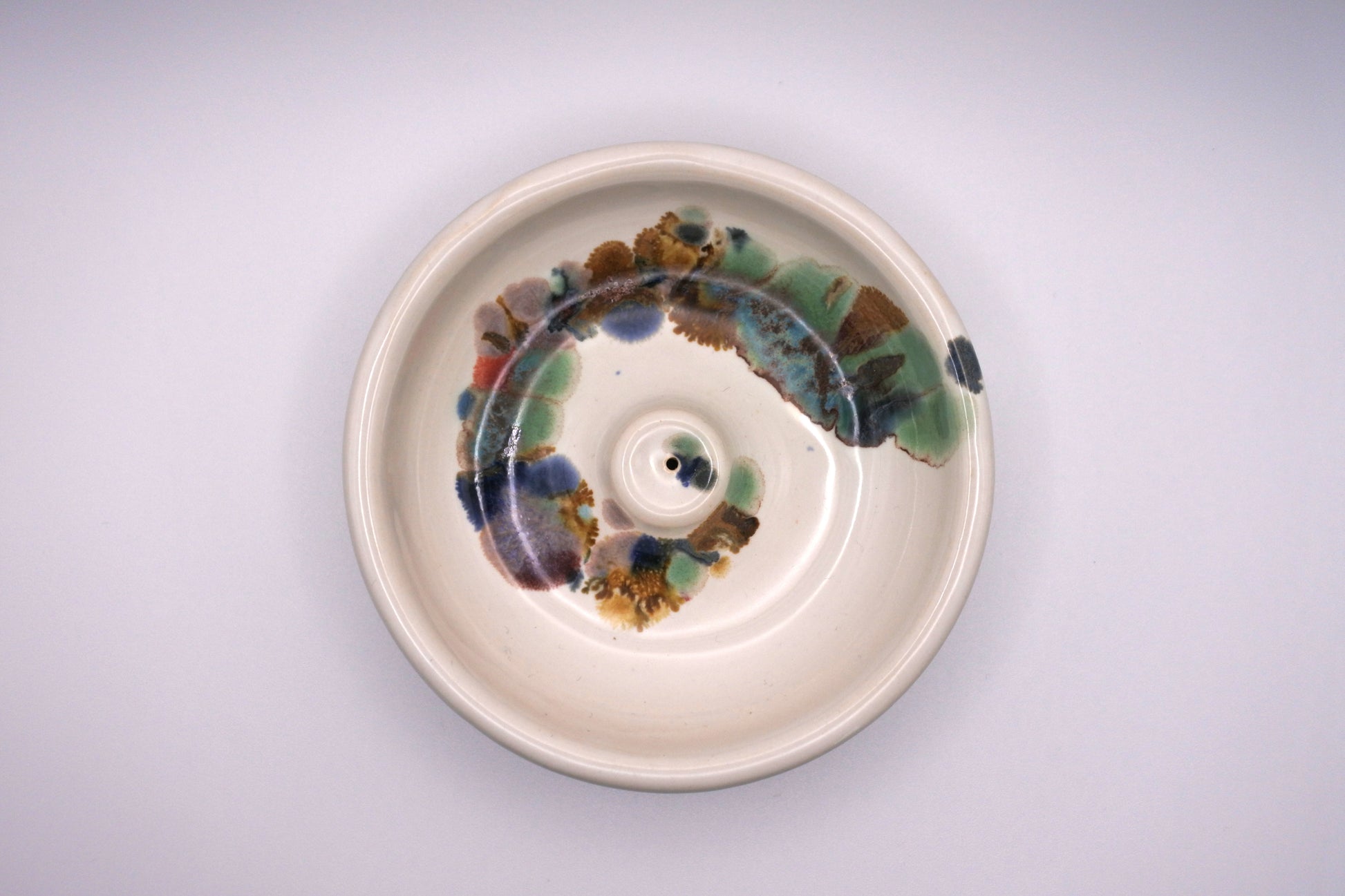 white circular incense burner with multi color drips in a spiral pattern