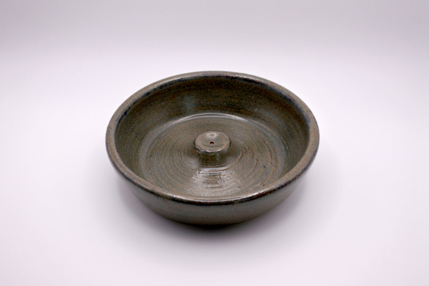 circular incense burner with textured surface in tones of forest green, olive, brown, and dark grey